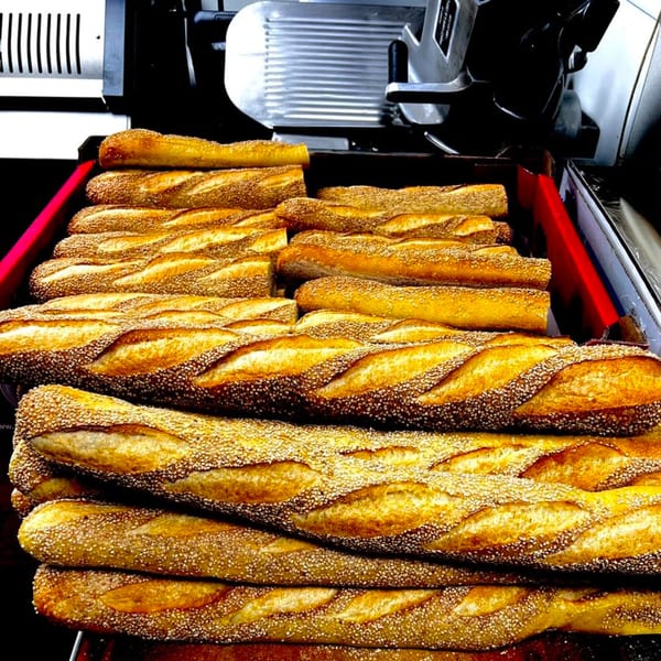 Golden-brown, sesame-crusted baguettes, ready for Stoli's Steaks cheesesteaks, stacked in a red tray.