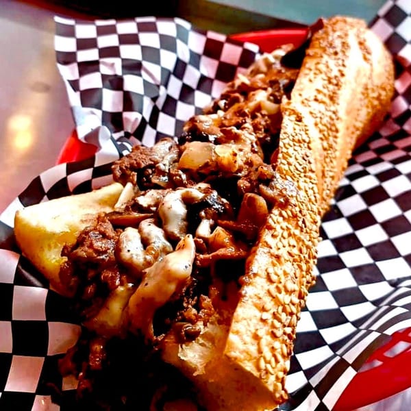 A Stoli's Steaks cheesesteak with melted cheese, onions, and mushrooms in a red basket.