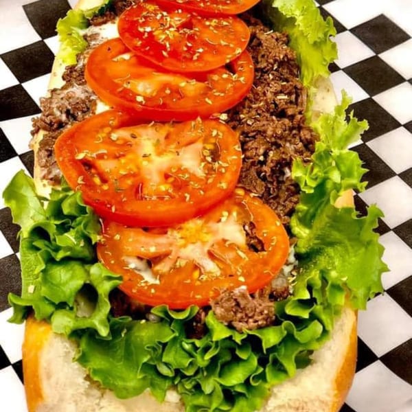 Stoli's Steaks cheesesteak with chopped steak, melted cheese, lettuce, and sliced tomatoes on a roll.