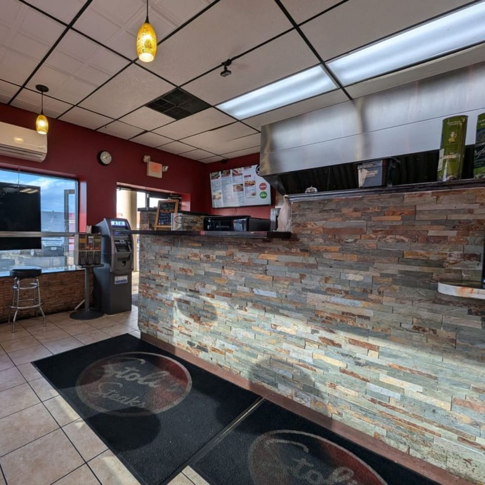 Interior of Stoli's Steaks, featuring a stone-faced counter, menu board, and branded floor mats.