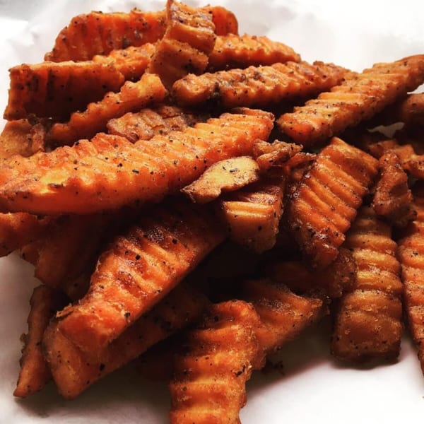 Close-up of crispy, crinkle-cut sweet potato fries seasoned with pepper from Stoli's Steaks.