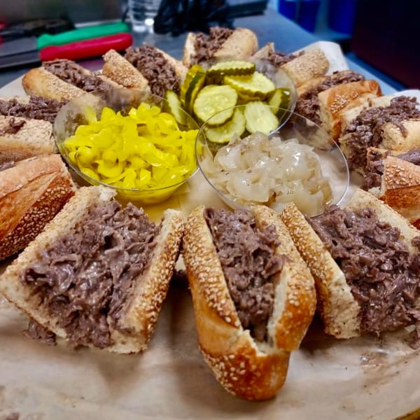 Stoli's Steaks cheesesteak platter with bowls of pickles, banana peppers, and onions.