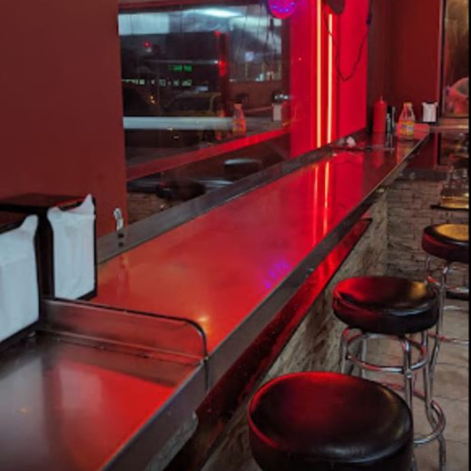Stoli's Steaks counter with red neon lighting, stools, and a view into the kitchen.