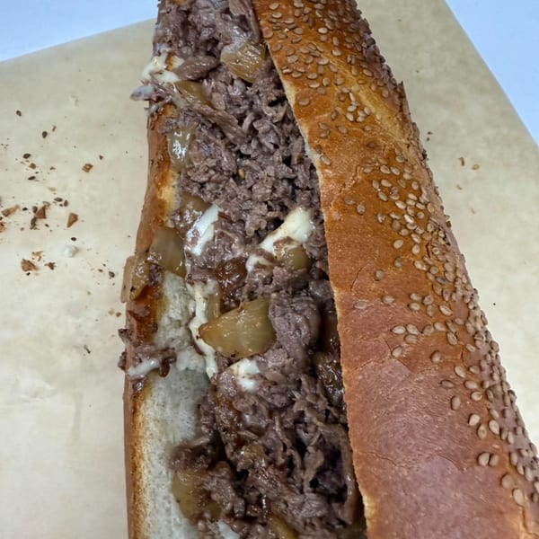 A Stoli's Steaks cheesesteak with melted cheese and onions on a sesame seed roll.