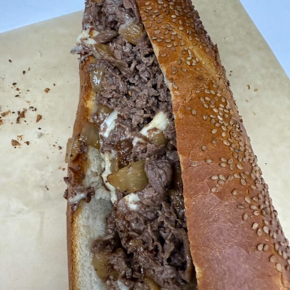 A Stoli's Steaks cheesesteak with melted cheese and onions on a sesame seed roll.