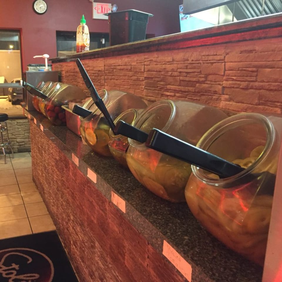 Pickle bar at Stoli's Steaks, featuring several large glass jars filled with various pickled vegetables.