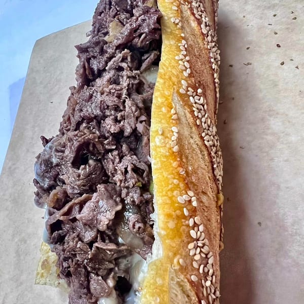 A Stoli's Steaks cheesesteak, with thinly sliced meat and cheese on a sesame seed roll.